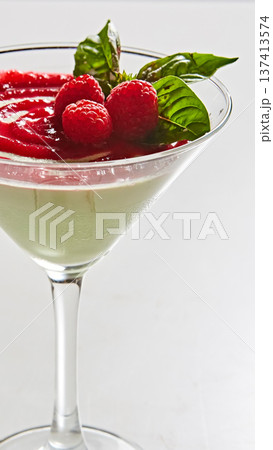 Gourmet panna cotta served in a martini glass with a vibrant raspberry coulis swirl and fresh mint 137413574