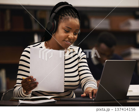 Woman, studying and headphones in library for research, documents and computer research or planning in university. African student reading paper, listening to music or laptop for focus and e learning 137414156