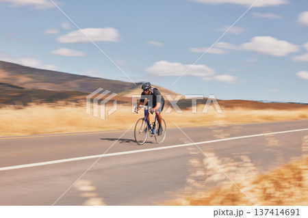 Road, nature and man cycling fast for workout, exercise and scenic mountain path with motion. Health, wellness and cyclist on speed bike for morning training, practice and bicycle race with blue sky. 137414691