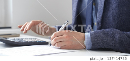 Professional accountant calculating expenses, documenting financial details on notepad while working at corporate desk. Audit and taxes in business Professional accountant calculating expenses, documenting financial details on notepad while working at corporate desk. Audit and taxes in business 137414786
