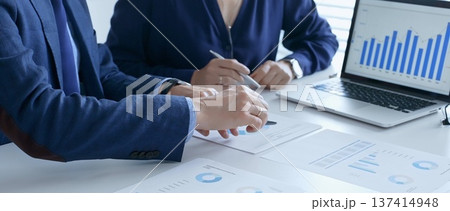 Business team analyzing financial data on a laptop and printed documents, pointing at charts and graphs during a meeting. Business people and finance concept 137414948