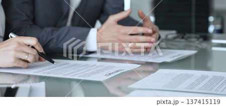 Business people reading and discussing contract terms, financial agreement, and legal paperwork during a negotiation. 137415119