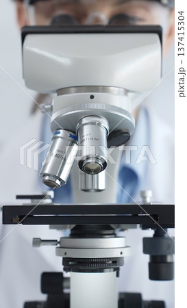 Scientist wearing lab coat and protective glasses using a modern microscope in a laboratory setting, conducting research and experiments in a scientific environment. Health care and science concept 137415304