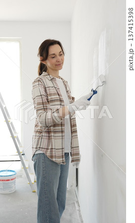 Woman wearing protective gloves rolling white paint onto wall, updating living space with fresh color and personal home renovation effort Woman wearing protective gloves rolling white paint onto wall, updating living space with fresh color and personal home renovation effort 137415398