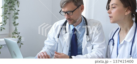 Two doctors are studying medical charts on a laptop, discussing patient data in a hospital or clinical setting. Medicine and healthcare concept. Two doctors are studying medical charts on a laptop, discussing patient data in a hospital or clinical setting. Medicine and healthcare concept. 137415400