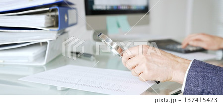 Male accountant holding magnifying glass, checking financial documents on office desk, analyzing taxes and data. Audit and taxes in business Male accountant holding magnifying glass, checking financial documents on office desk, analyzing taxes and data. Audit and taxes in business 137415423