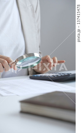 Businesswoman carefully reviewing financial reports using magnifying glass and calculator, close up vertical view. Audit and taxes in business Businesswoman carefully reviewing financial reports using magnifying glass and calculator, close up vertical view. Audit and taxes in business 137415478