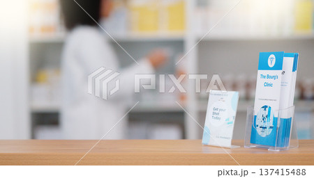 Focus on an information pamphlet on a counter at a pharmacy, advertising treatment and health care with a pharmacist packing rows medication on a shelf in a modern drugstore against blur background Focus on an information pamphlet on a counter at a pharmacy, advertising treatment and health care with a pharmacist packing rows medication on a shelf in a modern drugstore against blur background 137415488