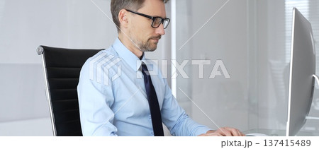 Mature businessman in office concentrating on important computer work, typing on keyboard, engaging in professional tasks, representing technology, development, and progress Mature businessman in office concentrating on important computer work, typing on keyboard, engaging in professional tasks, representing technology, development, and progress 137415489