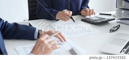 Business team analyzing financial documents, using calculators and laptop, working together on project in modern office. Audit and taxes concept 137415591