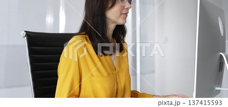 Businesswoman wearing yellow casual blouse and glasses is typing on laptop at office glass desk, analyzing data for business tasks. Audit in business Businesswoman wearing yellow casual blouse and glasses is typing on laptop at office glass desk, analyzing data for business tasks. Audit in business 137415593