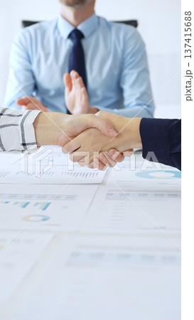 Business people shaking hands in office with financial charts, laptop and reports on table, symbolizing success, teamwork, agreement and corporate growth. Handshake concept 137415688