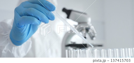 Scientific researcher wearing protective gear, carefully pipetting liquid into test tubes while conducting medical research experiment in laboratory. Medicine, healthcare and science concept Scientific researcher wearing protective gear, carefully pipetting liquid into test tubes while conducting medical research experiment in laboratory. Medicine, healthcare and science concept 137415703
