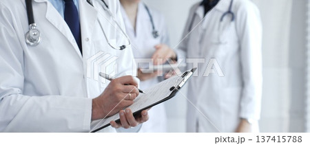 During a discussion with the medical team, a physician takes notes on a clipboard, capturing aspects of collaborative patient care, documentation, and clinical healthcare strategies 137415788