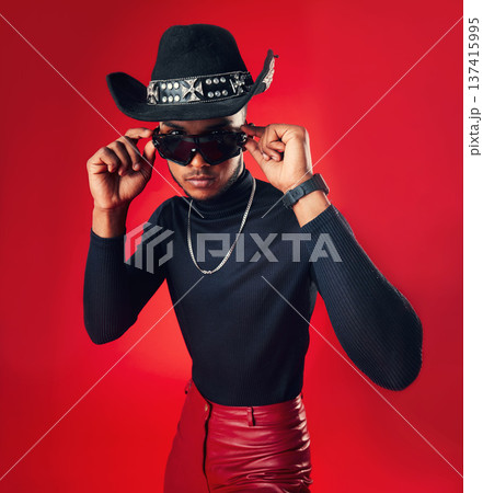 Fashion, man and cowboy hat, sunglasses and trendy clothes with gen z isolated on red background. Confident model, cool and leather pants with eyewear accessory, western aesthetic and edgy in studio 137415995