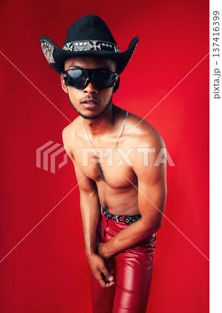 Fashion, man and cowboy hat, sunglasses and shirtless, clothes and gen z isolated on red background. Confident model, cool and leather pants with eyewear accessory, western aesthetic in a studio Fashion, man and cowboy hat, sunglasses and shirtless, clothes and gen z isolated on red background. Confident model, cool and leather pants with eyewear accessory, western aesthetic in a studio 137416399