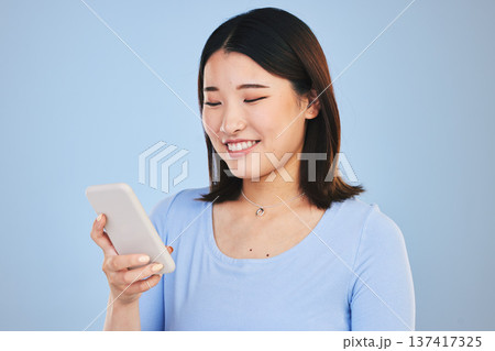 Happy asian woman, phone and typing in social media, networking or communication against a blue studio background. Female person smile in online research, chatting or texting on mobile smartphone app Happy asian woman, phone and typing in social media, networking or communication against a blue studio background. Female person smile in online research, chatting or texting on mobile smartphone app 137417325