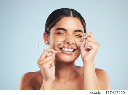 Woman, smile and floss teeth in studio for dental hygiene, care and gum gingivitis on blue background. Happy female model cleaning mouth with oral thread for fresh breath, healthy habit and grooming Woman, smile and floss teeth in studio for dental hygiene, care and gum gingivitis on blue background. Happy female model cleaning mouth with oral thread for fresh breath, healthy habit and grooming 137417490