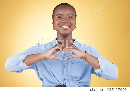 Happy black woman, portrait and heart hands for support, love or care against a yellow studio background. Face of African female person smile with loving emoji, shape or symbol icon on valentines day 137417991