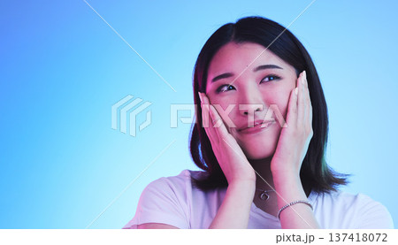 Face, thinking and Asian woman with beauty or dream with hope or smile isolated in a studio blue background. Cute, shy and happy young female person with skincare or soft skin and with a memory 137418072