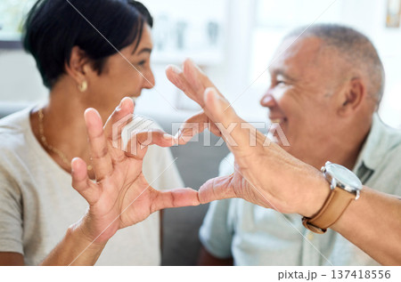 Heart shape, hands and senior couple bonding and talking in the living room of their home. Happy, smile and closeup of an elderly man and woman in retirement with a love sign or gesture together. Heart shape, hands and senior couple bonding and talking in the living room of their home. Happy, smile and closeup of an elderly man and woman in retirement with a love sign or gesture together. 137418556