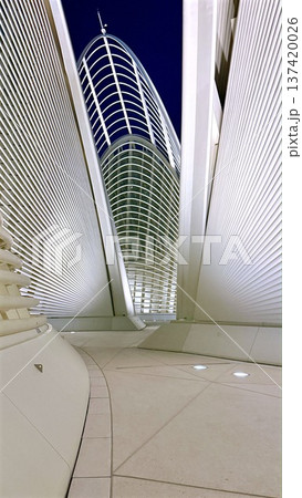Elegant Curved Corridor With Illumination. Sleek Curving Hall Stretching Towards Luminous Tower Beneath Peaceful Nocturnal Ambiance With Clean Flooring And Gentle Ground Lights 137420026