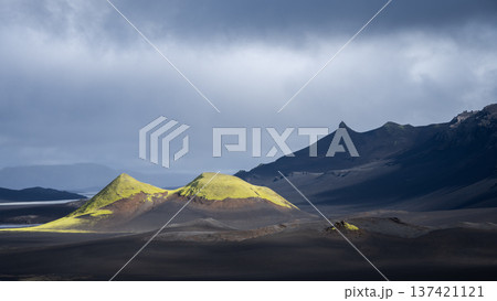 Black volcanic landscape with cloudy sky and two green illuminated mountains , Highlands Iceland Black volcanic landscape with cloudy sky and two green illuminated mountains , Highlands Iceland 137421121