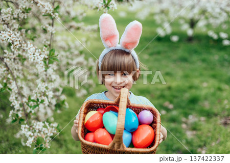 Easter egg hunt. child Wearing Bunny Ears Running To Pick Up Egg In Garden. Easter tradition. Baby with basket full of colorful eggs. Easter egg hunt. child Wearing Bunny Ears Running To Pick Up Egg In Garden. Easter tradition. Baby with basket full of colorful eggs. 137422337