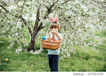 Easter egg hunt. child Wearing Bunny Ears Running To Pick Up Egg In Garden. Easter tradition. Baby with basket full of colorful eggs. 137422339