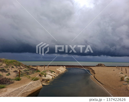 The Mediterranean Sea shows layered low clouds before Hurricane Dana. A stream flows into the sea while sandy beach stretches on the shore. People may be preparing for the storm. The Mediterranean Sea shows layered low clouds before Hurricane Dana. A stream flows into the sea while sandy beach stretches on the shore. People may be preparing for the storm. 137422626