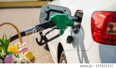 Car refueling with green fuel nozzle beside basket of Easter eggs and tulips outdoors. spring travel, holiday transport, Easter 137423152