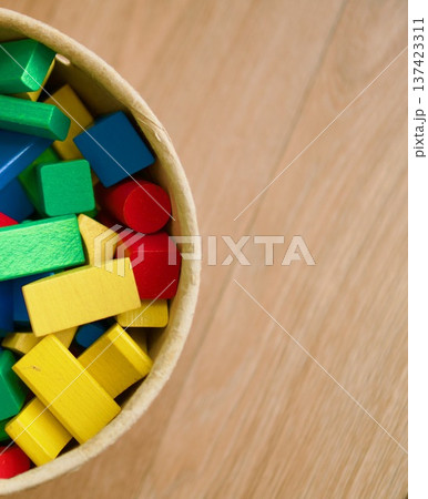 Colorful wooden toy blocks in a round container on a light wooden background, 137423311