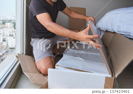 Man unpacking flat-pack furniture box for home assembly Man unpacking flat-pack furniture box for home assembly 137423401