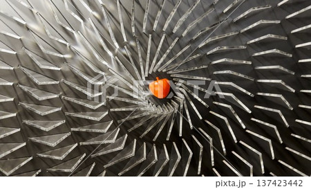 Top view on spiral geometric installation with metallic radial elements surrounding a red apple-shaped object in the center. Strong symmetry, depth and optical movement create a striking visual focus 137423442