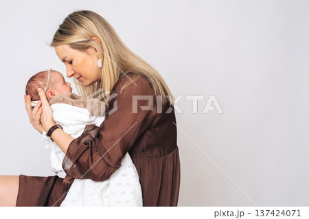 Portrait of caring mother hugging newborn baby girl. Concept of motherhood, parenting, love and family happiness, perfect for Mothers Day themes. 137424071