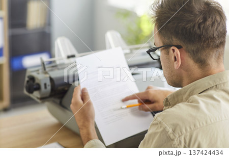 Close-up of man proofreading page with pencil beside vintage typewriter in office 137424434