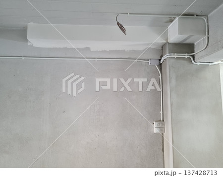 Electrical conduits and wiring installation on unfinished concrete walls and ceiling. Interior construction site with junction box plus sockets. Industrial building renovation or site maintenance. 137428713