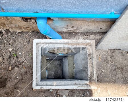 Concrete drainage manhole installation in the ground with blue PVC pipes connected. Square precast concrete pit for sewer system or water management during residential house construction. Concrete drainage manhole installation in the ground with blue PVC pipes connected. Square precast concrete pit for sewer system or water management during residential house construction. 137428714
