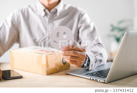 Shopping customer experience concept, person holding happy face icon, showing satisfaction for online delivery service, positive feedback review with received box, laptop on desk Shopping customer experience concept, person holding happy face icon, showing satisfaction for online delivery service, positive feedback review with received box, laptop on desk 137431412