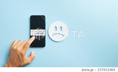 Experience poor customer service, hand inputs negative online review on mobile phone, displaying one star feedback rating for low satisfaction, with prominent unhappy face 137431464
