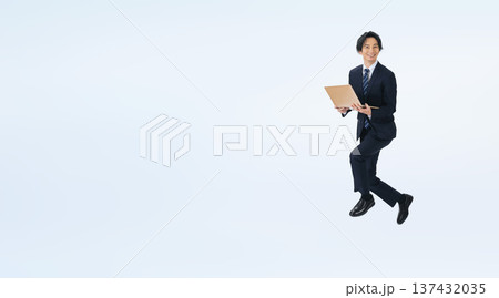 パソコンを使いながらジャンプする男性ビジネスパーソンの全身写真 パソコンを使いながらジャンプする男性ビジネスパーソンの全身写真 137432035