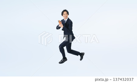 スマホを使いながらジャンプする男性ビジネスパーソンの全身写真 スマホを使いながらジャンプする男性ビジネスパーソンの全身写真 137432037
