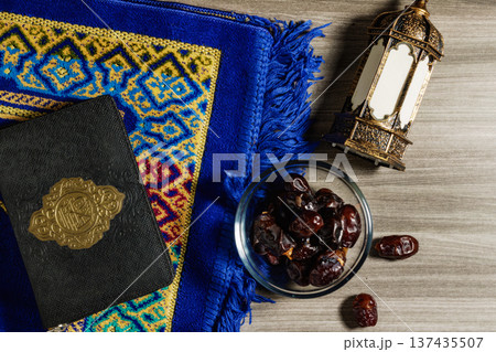 Ramadan Flat Lay with Holy Quran, Bowl of Dates, and Golden Lantern on Blue Prayer Rug over Wooden Background. High quality photo 137435507