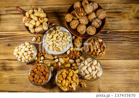 Assortment of nuts on wooden table. Almond, hazelnut, pistachio, peanut, walnut and cashew in small bowls. Top view. Healthy eating concept Assortment of nuts on wooden table. Almond, hazelnut, pistachio, peanut, walnut and cashew in small bowls. Top view. Healthy eating concept 137435670