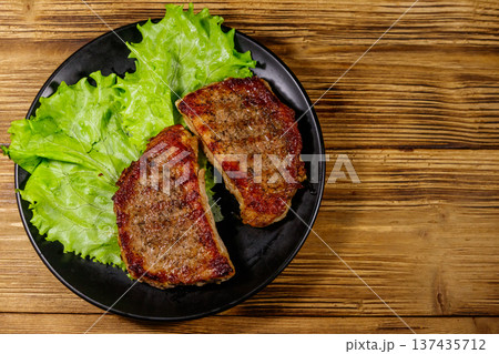 Grilled pork steaks with lettuce leaves on wooden table. Top view 137435712