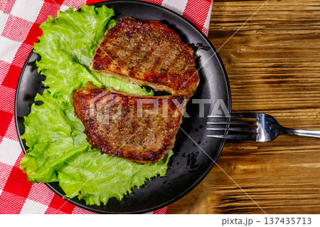 Grilled pork steaks with lettuce leaves on wooden table. Top view 137435713