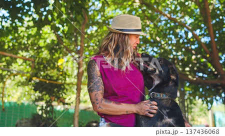 Tattooed woman wearing hat bonding with dog in sunny park Tattooed woman wearing hat bonding with dog in sunny park 137436068