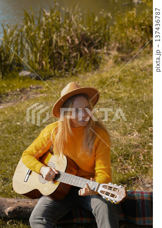 Portrait of smiling caucasian artist plays wooden acoustic guitar in autumnal park. Young songwriter plays string musical instrument hobby outside in nature fall time. Audio music healing Portrait of smiling caucasian artist plays wooden acoustic guitar in autumnal park. Young songwriter plays string musical instrument hobby outside in nature fall time. Audio music healing 137436787