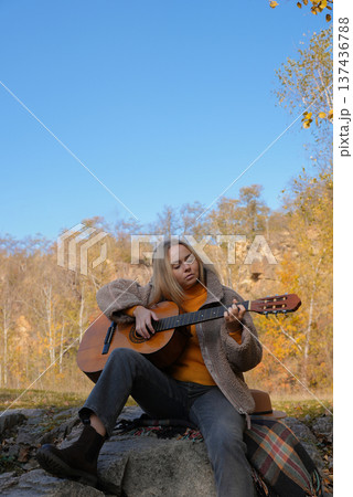 Blonde woman playing string guitar outdoors in autumn forest. Concept of sound therapy, mental health and wellness rituals. Calmness tranquility audio-sensory practices. Aura farming energy Blonde woman playing string guitar outdoors in autumn forest. Concept of sound therapy, mental health and wellness rituals. Calmness tranquility audio-sensory practices. Aura farming energy 137436788