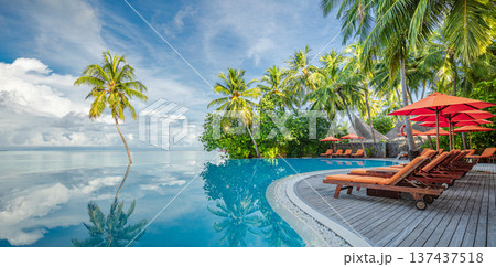 Panoramic holiday landscape. Luxurious beach resort hotel swimming pool and beach chairs or loungers under umbrellas with palm trees, blue sunny sky. Summer island seaside, travel vacation background 137437518